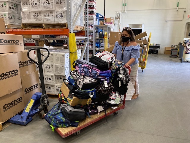 An RRPS employee pushes a cart full of donated backpacks in our warehouse