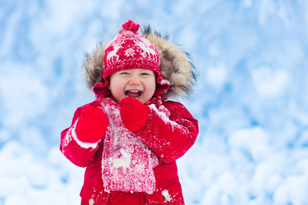 Small child in a red coat and gloves playing in the snow.